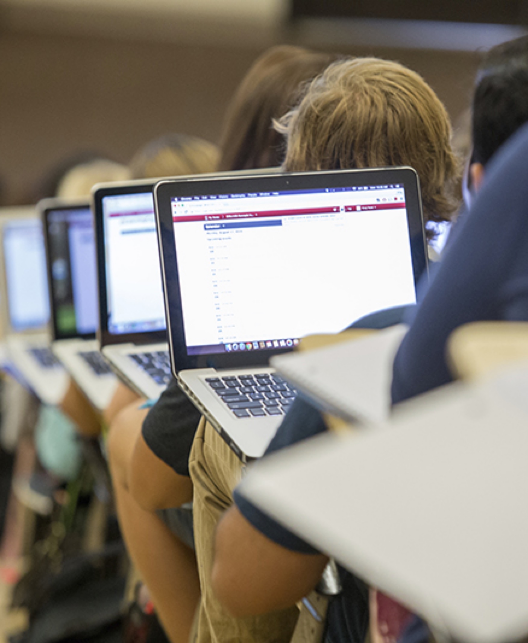 Students are sitting in a lecture hall on campus. The laptop screens of the students are visible in the image.